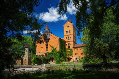 an ancient castle among green trees against a background of blue sky and white clouds