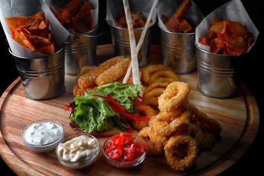 beer snacks. chips, squid rings, croutons and nuggets, with sauces, on a wooden board