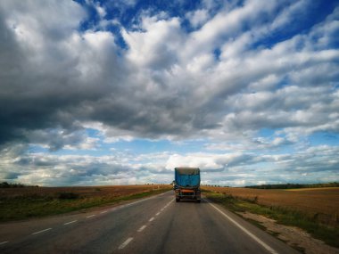 trucks is driving on the highway, among fields, blue sky with clouds