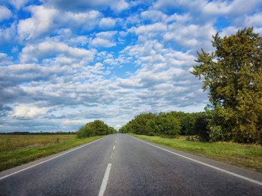 Summer empty road, highway. Green trees, fields and meadows, white clouds and blue sky