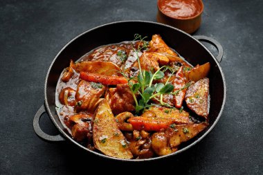 Soslu kızarmış patates, mantarlı ve sebzeli, bir tavada, koyu betonda.