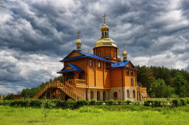 Ormanın kenarında, bulutlu bir gökyüzüne karşı gün ışığıyla aydınlatılan ahşap kilise.
