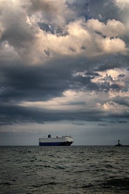 Limandan büyük gemi kalkıyor. dramatik bulutlar. Deniz feneri. dikey