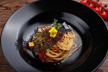 Siyah tabakta kiraz domatesli iştah açıcı spagetti ve ahşap arka plan.