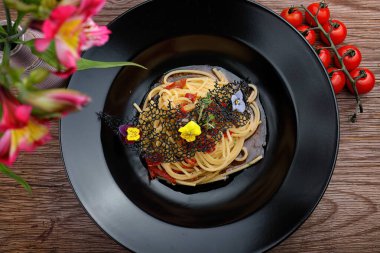 Siyah tabakta kiraz domatesli iştah açıcı spagetti ve ahşap arka plan.