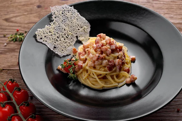 黑盘上夹着脆咸肉和樱桃番茄的意大利面 — 图库照片
