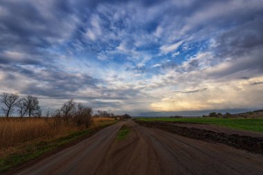 İlkbahar, yağmur, kırsal yol. Bulutlar ve mavi gökyüzü