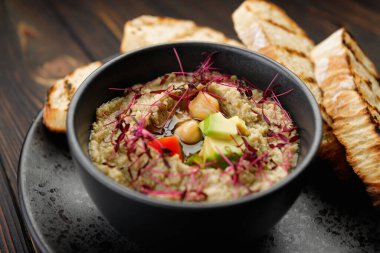Avokado ve domatesli humus, siyah bir tabakta ekmek kızartma, ahşap bir arka planda.