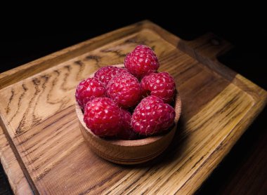 Yeni toplanmış ahududular siyah arka planda ahşap bir yüzey üzerinde sergilenir.