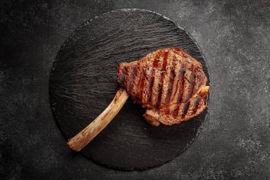 Kızarmış biftek, siyah yuvarlak bir taşın üzerinde, koyu bir arka planda.