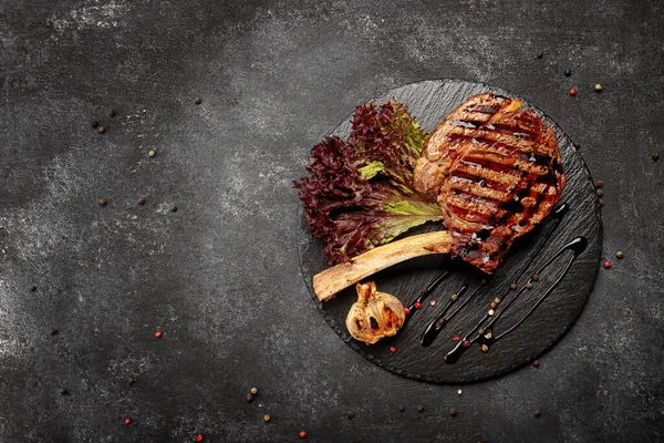 Kızarmış biftek, siyah yuvarlak bir taşın üzerinde, koyu bir arka planda.