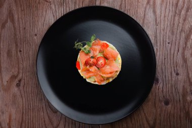 Kahvaltı, çırpılmış yumurtalı ekmek, somon, avokado ve domates, siyah bir tabakta.