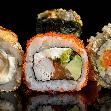 Siyah bir arkaplanda yansımalı suşi ruloları.