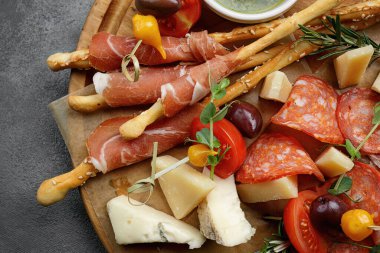 Lezzetli peynir, sosis, ekmek ve Grissini seçimi ahşap bir tahtanın üzerinde güzelce sergilenmiştir.