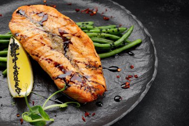 Siyah tabakta kuşkonmaz ve limonlu kızarmış somon bifteği.