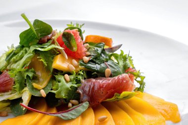 Karışık mango salatası, kurutulmuş et, greyfurt, çam fıstığı ve nane, beyaz bir tabakta, beyaz arka plan
