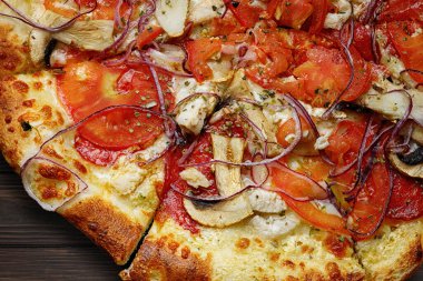baked pizza with chicken, mushrooms, tomatoes, onions and cheese, on a wooden board