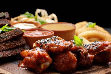 Tahta üzerinde farklı soslar bulunan çeşitli bira aperatifleri. Kalamar, mangal kanatları, sarımsaklı kızarmış ekmek.
