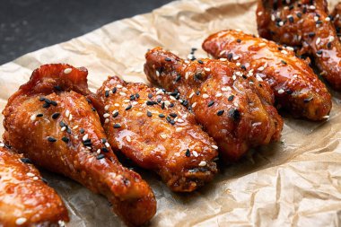 Parşömen üzerinde baharatlı sosla kızartılmış tavuk, koyu bir arka planda.