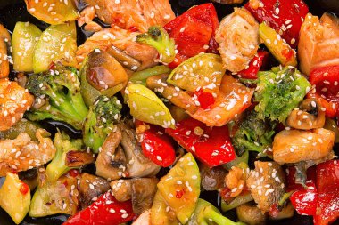 Somon parçaları, sebze, mantar ve susam, siyah bir zemin üzerine bir tavada balık salatası