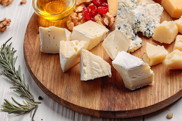 Pieces of various cheeses with nuts, herbs and honey, on a white wooden background