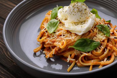 Pasta with stewed vegetables and mozzarella on a plate on a wooden background