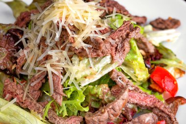 Beyaz tabakta et ve peynirli sıcak salata.