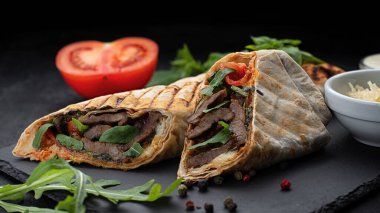 Shawarma et, peynir, domates ve sosla birlikte siyah bir arka planda.