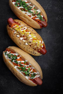 Three hotdogs with different fillings and different sausages on gray concrete