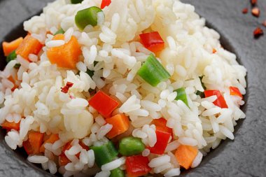 Siyah bir arka planda, siyah bir tabakta sebze ve baharatlı risotto.