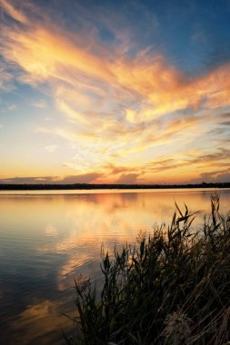 Gölde gün batımı, sazlıklar, yansımalar ve renkli bulutlar.