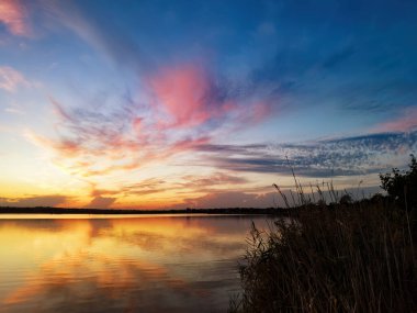 Gölde gün batımı, sazlıklar, yansımalar ve renkli bulutlar.