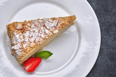 Bir parça kek Napolyon, beyaz bir tabakta, çilekli ve naneli, koyu bir arka planda. en üstteki görünüm