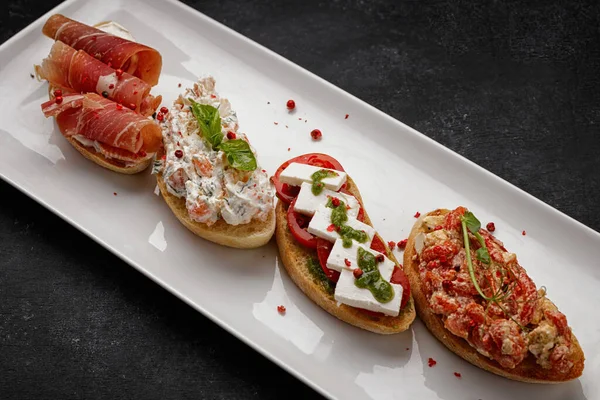 Jambonlu, deniz mahsullü, sebzeli ve peynirli, koyu betonda farklı bruschetta.