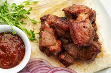 Lavaş, sos, mikroyeşil ve soğanlı kızarmış şiş kebap.