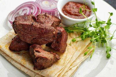 Lavaş, sos, mikroyeşil ve soğanlı kızarmış şiş kebap.
