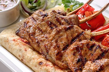 Domuz eti, kuzu kaburgası, pide ekmeği, fırında dolma biber ve sos, beyaz bir tabakta, beyaz arka planda.