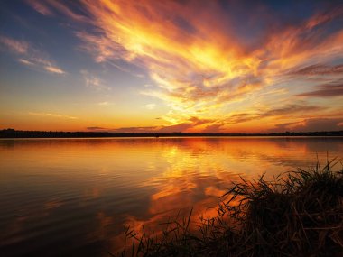 Gölün kıyısında, ön planda kamışlarla baş döndürücü bir gün doğumu.