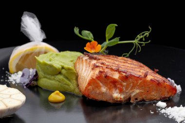 Limonlu siyah bir tabakta kızarmış somon parçası. Biftek. Fileto