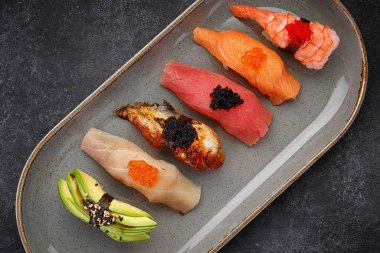 Nigiri suşisi tabakta, koyu betonda. Üst görünüm