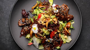 Sıcak salata, dana eti ve mantarlı, tabakta, koyu betonda.