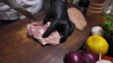 Aşçı ahşap bir tahtada tavuk budu keser.