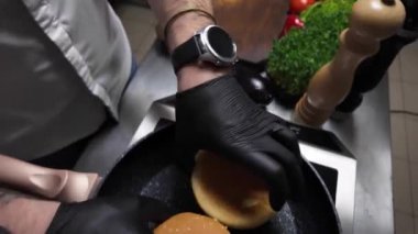 Profesyonel erkek aşçı kızarır ve kızgın ızgarada dilimlenmiş çöreğe dönüşür. Lokanta mutfağında lezzetli hamburgerler pişirmek. Malzemelerin hazırlanması. Lezzetli ev yapımı hamburgerlerle barbekü.