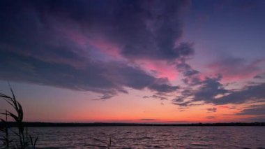 Gölde huzurlu bir günbatımı. Renkli bulutlar, sudaki yansımalar. Yavaş çekim
