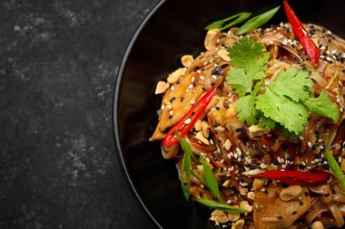 Tavuklu ve sebzeli erişte, siyah bir tabakta, arka planda.