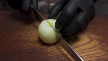 Siyah eldivenli bir adam tahta bir tahtanın üzerinde soğan doğruyor.