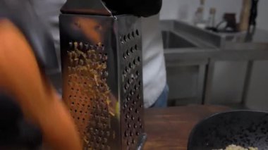 Bir adam metal rendesinde çiğ havuç rendeliyor.