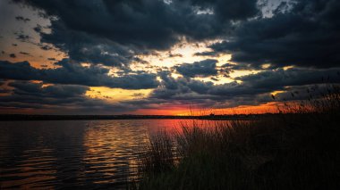 Gölde dramatik bir gün batımı, güneş ışığı ve bulutlar