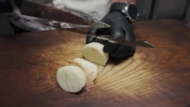 Siyah eldivenli eller tahtadan soğan kesiyor.