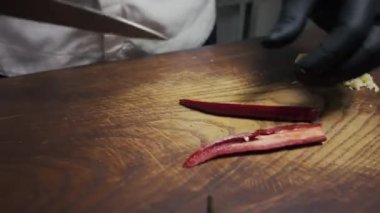 Siyah eldivenli eller ahşap bir tahtada acı kırmızı biber kesti.